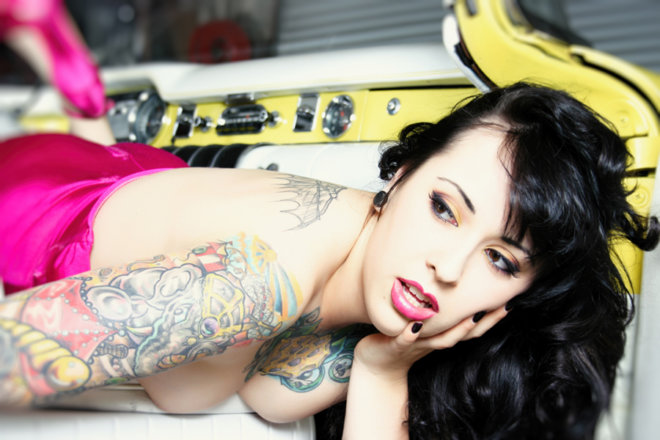 Tattooed brunette woman leaning out of vintage yellow Buick car